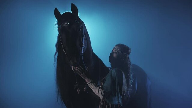 women artist stroking a black thoroughbred horse under beautiful lighting in the circus