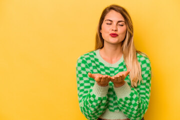 Young caucasian woman isolated on yellow background folding lips and holding palms to send air kiss.