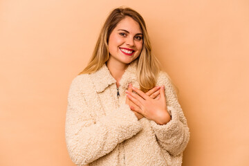 Young caucasian woman isolated on beige background has friendly expression, pressing palm to chest. Love concept.