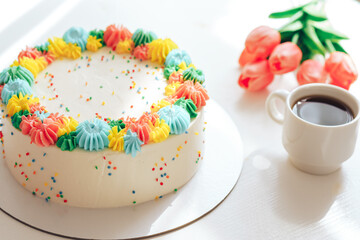 White cake decorated with multi-colored cream next to tulips and coffee.