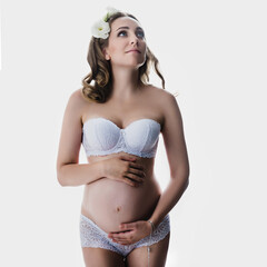 Pregnant woman in white lace lingerie posing at photostudio on white background