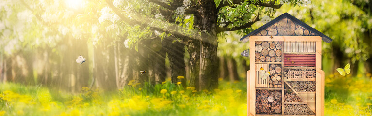 Beautiful insect hotel with flying butterflies and bees in a sunny summer orchard © Martin Bergsma
