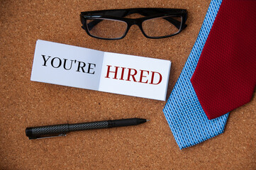 You are hired text on notepad with neckties, pen and glasses background. Employment concept