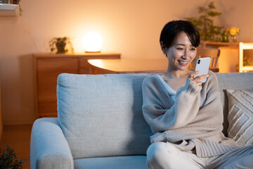 Obraz premium 夜に家でリラックスする女性（スマホ・メール・インターネット）