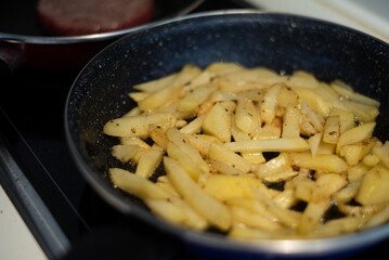 Cooking meat and fries in oily saucepan   