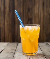 Orange soda in a glass with ice and straw over wooden table