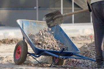 Worker at the construction site loads the gravel with shovel in the wheelbarrow