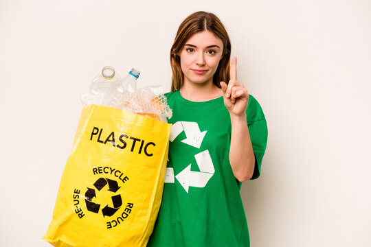 Young woman holding a bag full of plastic bottles to recycle isolated on white background showing number one with finger. - Powered by Adobe