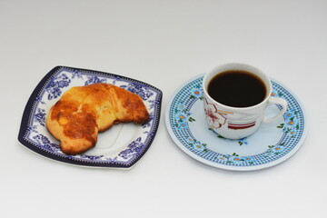 Breakfast -  porcelain platte  with croissant  and a cup of coffee  on black background