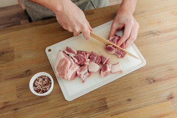 Man cutting meat with a knife on a cutting board. Wooden table. Fresh pork meat. Top view