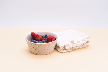 fresh organic strawberries and blueberries in a bowl with table napkin on a beige surface