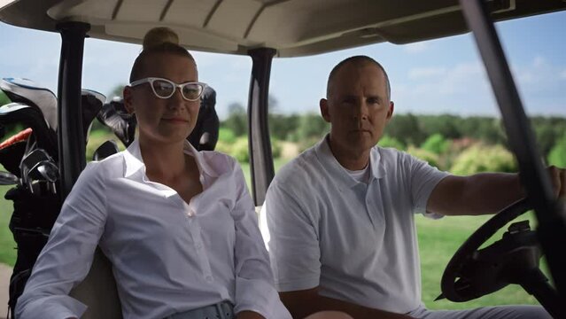 Golf players looking camera at cart. Couple sitting buggy on club course field.