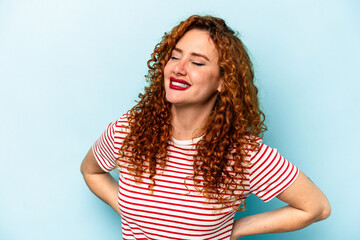 Young ginger caucasian woman isolated on blue background laughs happily and has fun keeping hands...