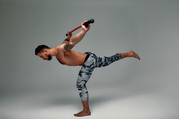 A ninja man holds on to a fighting stick and attacks close-up on gray studio background