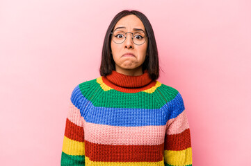 Young hispanic woman isolated on pink background shrugs shoulders and open eyes confused.