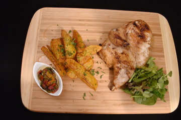 chicken breast with fried potatoes salad and spicy spices on a wooden plate