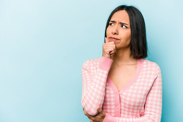Young hispanic woman isolated on blue background looking sideways with doubtful and skeptical expression.