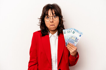 Young business hispanic woman holding banknotes isolated on white background shrugs shoulders and...