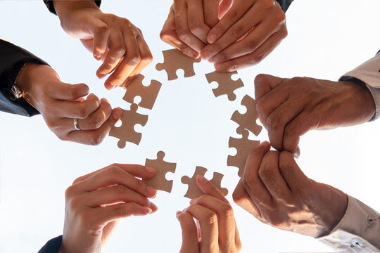 The Hand Of A Businessman Holding A Paper Jigsaw And Solving The Puzzle Together. The Business Team Assembles A Jigsaw Puzzle. A Business Group Wishing To Bring Together The Puzzle Pieces