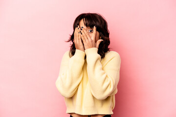 Young hispanic woman isolated on pink background blink through fingers frightened and nervous.