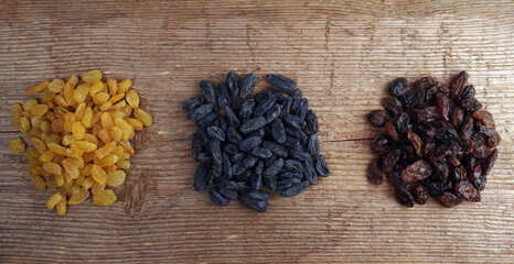 Three heaps of raisins of various varieties on a rough wooden background texture.