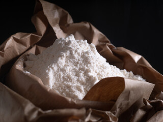 Paper bag, sack, with flour against dark background