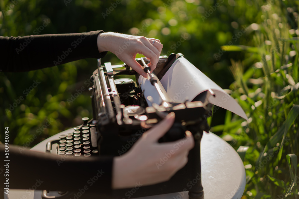 Fototapete hands loading paper into a retro typewriter with blank sheet. dream writer's workplace in green whea