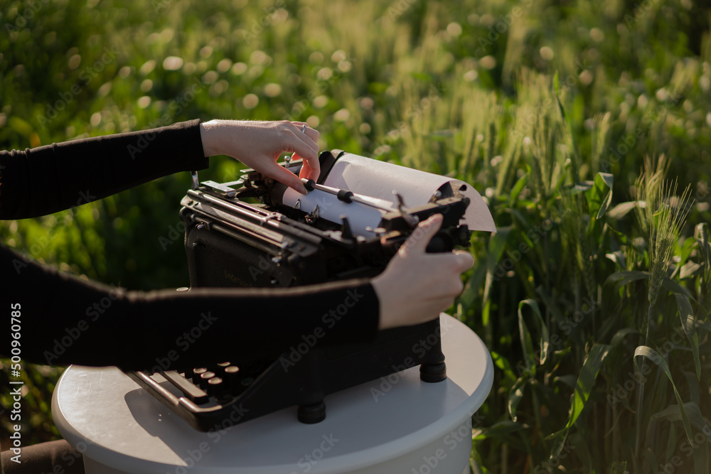 Fototapete hands loading paper into a retro typewriter with blank sheet. dream writer's workplace in green whea