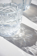 primer plano de un vaso de cristal con agua y su sombra sobre una mesa blanca