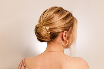 The concept of style, style and beauty. .Photo of a girl from the backside, with a pearl clip in her blonde hair, gathered in a neat bun, on a white studio background. Hairstyle for girls. Close-up