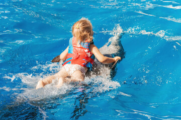 A happy girl rides a dolphin. The child is wearing a life jacket. Healthy lifestyle