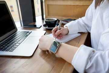 a woman in a white shirt writes a to-do list at her desk with a laptop phone and coffee close-up.