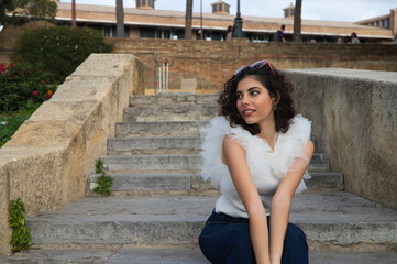 beautiful young woman with dark, curly hair sitting on a staircase in a park. The woman makes different expressions. Concept expressions. smiling, sad, thinking, enjoying, living.