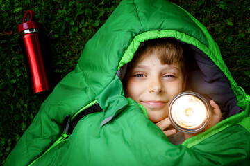 Preteen school kid boy in sleeping bag camping. Outdoors activity with children in summer. Fun and...