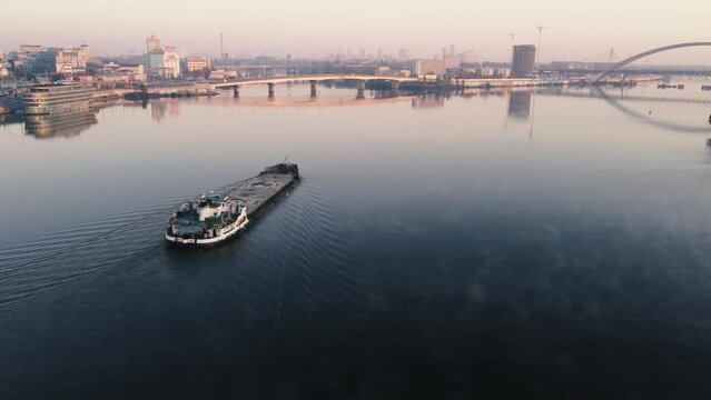 cargo barge floats on the river, morning haze, fog over the water. the copter flies over the cargo riverboat in the afternoon. drone filming from above the river in the city