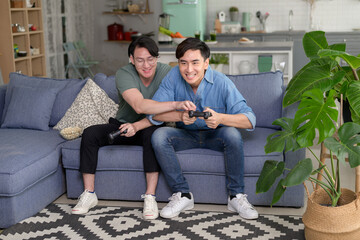 Young smiling gay couple playing video games in the living room at home, LGBTQ and diversity