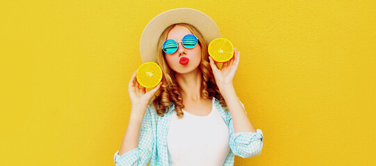 Summer portrait of happy young woman blowing her lips with slices of fresh orange fruits wearing straw hat, sunglasses on yellow background