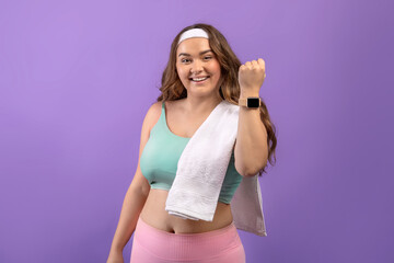 Glad young european plus size female in sportswear with towel show fit tracker after workout