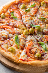 Sliced tasty fresh pizza with cheese, mozarella, olive, onion, tomatoes, spices and basil. Vegeterian italian pizza on wood cutting board