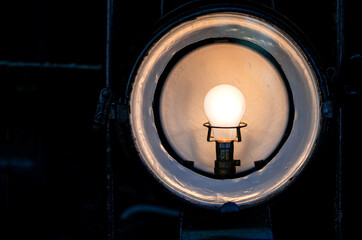Headlight lamp of a historic old steam engine locomotive with glowing electrical bulb and white round enamel reflector and vintage socket. Detail of oldtimer railway in a workshop depot in Germany.