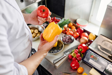 Close-up of professional cook choosing fresh vegetables for salad standing at kitchen table