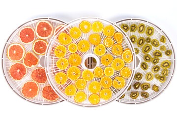 sliced pieces of fruit kiwi, orange, grapefruit, on round grates after drying, in special equipment, on a white table