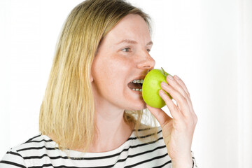 Young woman with dental braces biting green apple isolated light background. Studio. Cute lovely girl with metal braces on white clear teeth smiling in clinic. Close Up. Positive Emotion. Stomatology