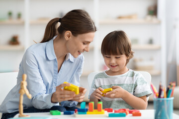 Obraz premium Games and education. Professional woman teacher exercising with little boy, playing wooden development toy at classroom