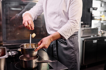 Close-up of chef in apron throwing butter in bowl and melting it on cooker to prepare a dessert