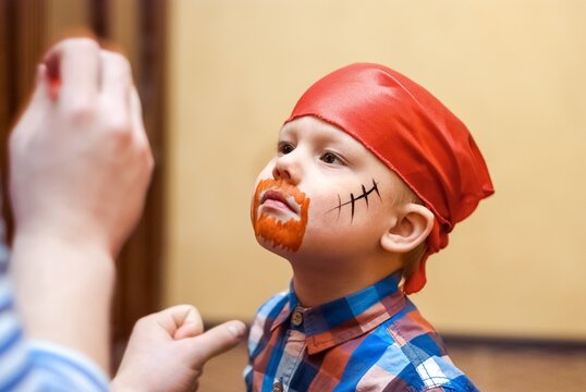 Animator makes pirate painting on face of toddler at children birthday party. Cute boy in red bandanna prepares for celebration close view