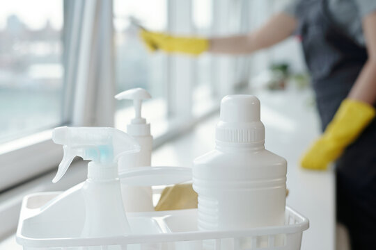 Three plastic bottles containing detergents for washing windows on sill against young worker of cleaning company carrying out work
