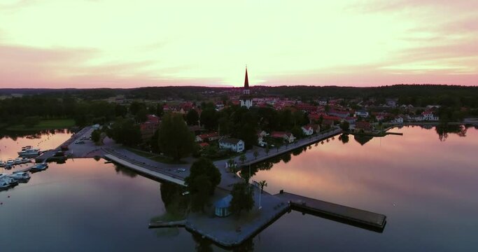 Aerial Shot Of Clock On Religious Structure Against Cloudy Sky, Drone Flying Forward Over Houses At Sunset - Mariefred, Sweden