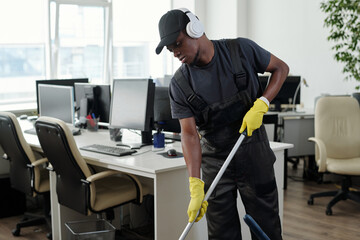 Young male staff of cleaning service company in headphones washing floor in large openspace office...