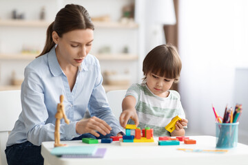 Fototapeta premium Cute little boy preschooler playing developing wooden games with professional woman psychologist at kindergarten